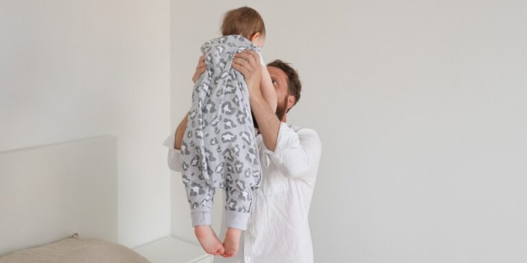 vater-haelt-kind-in-schlafsack-mit-fuessen-hoch